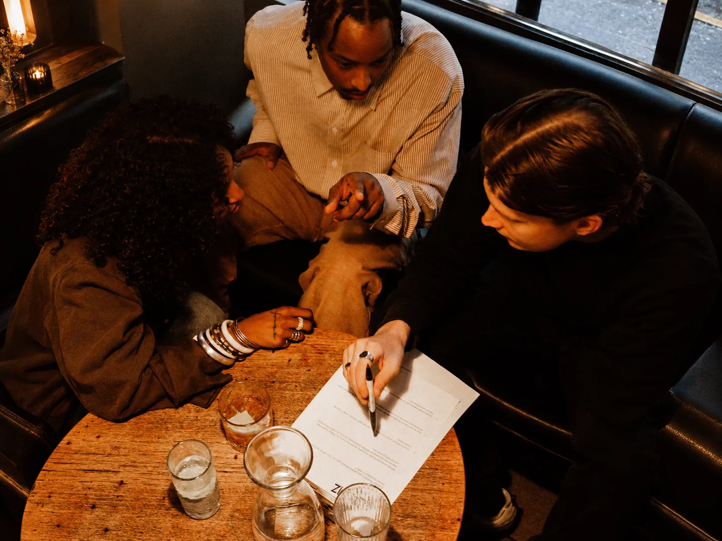 Three people discussing quiz answers and writing on a player sheet