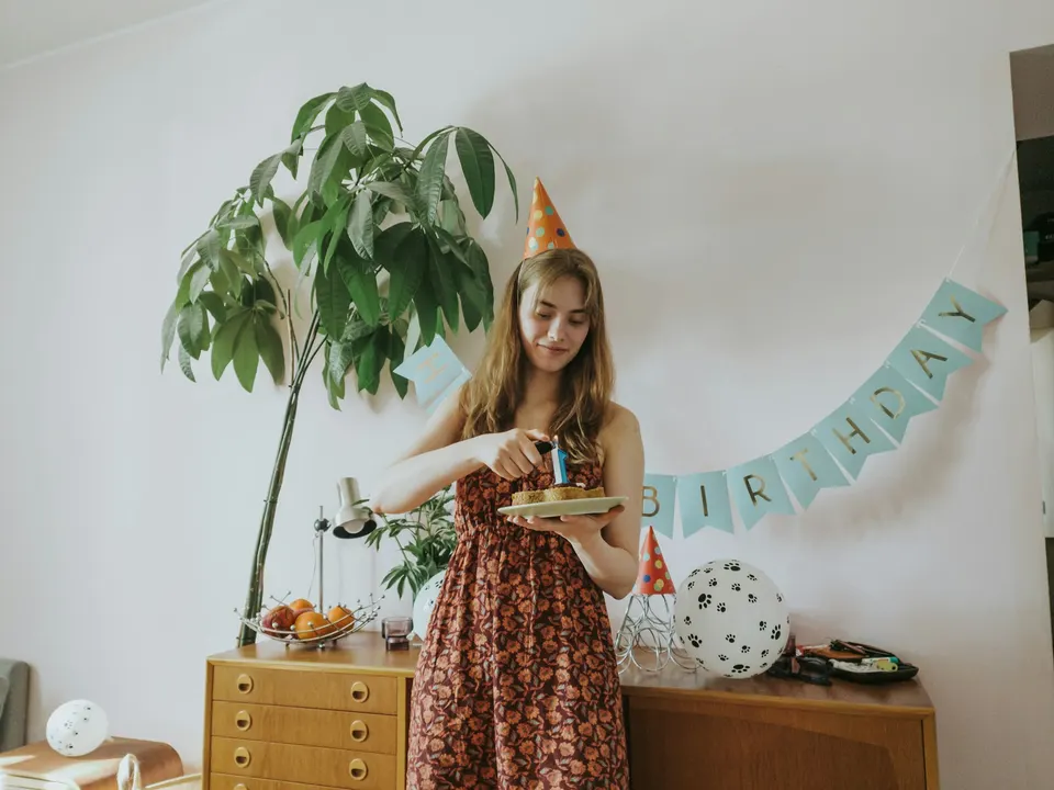 A woman wearing a party hat lighting a candle on her birthday cake